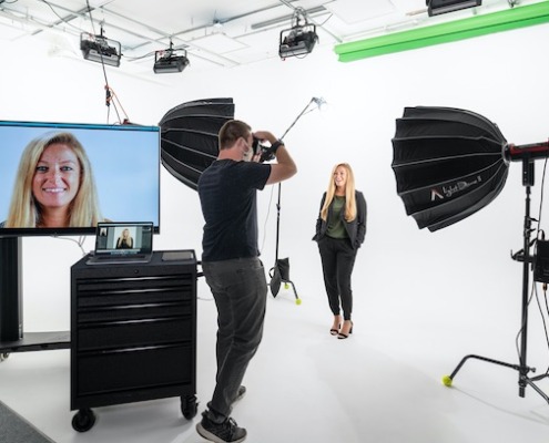 Professional Headshots Photographer taking headshot of woman on white cyclorama wall with lights and a monitor on set