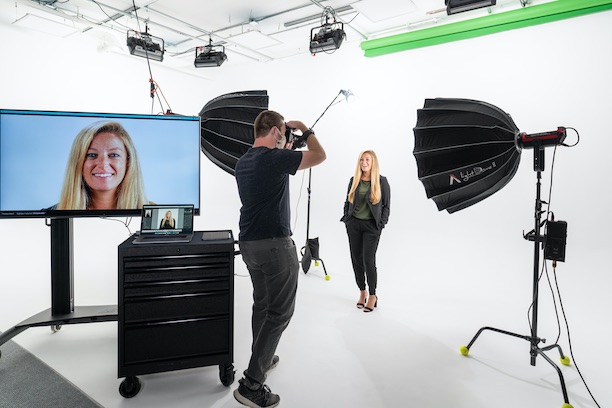 Photographer taking headshot of woman on white cyclorama wall with lights and a monitor on set