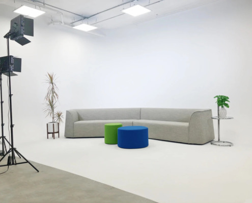 Set Pieces Available for Video Productions Grey couch on white cyc wall with lighting, plants, and a side table
