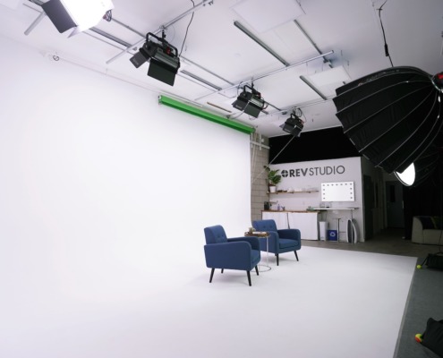 Our Studio is Your Blank Canvas Wide view of REV studio with cyclorama wall, green screen, lighting, and two blue chairs