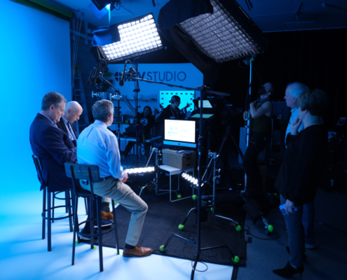 Three executives filming professional video content for business on a blue-lit set at REV Studios.