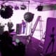 Photography shoot in progress at REV Studios with models on the cyc wall, professional lighting, and a production team, all under magenta lighting.