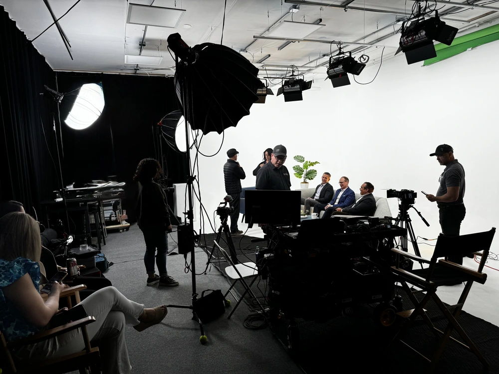 A professional film crew filming a talk show or podcast interview on a white cyclorama wall set at REV Studios.