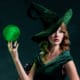 Portrait of a woman dressed as a velvet green witch holding a glowing, green, crystalline orb in her hand.